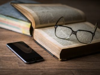 Smartphone with glasses and a book illustrating the launch of a Stack Overflow extension for the GitHub Copilot AI assistant for developers, enabling users to access the vast knowledge platform to find solutions for software development problems.